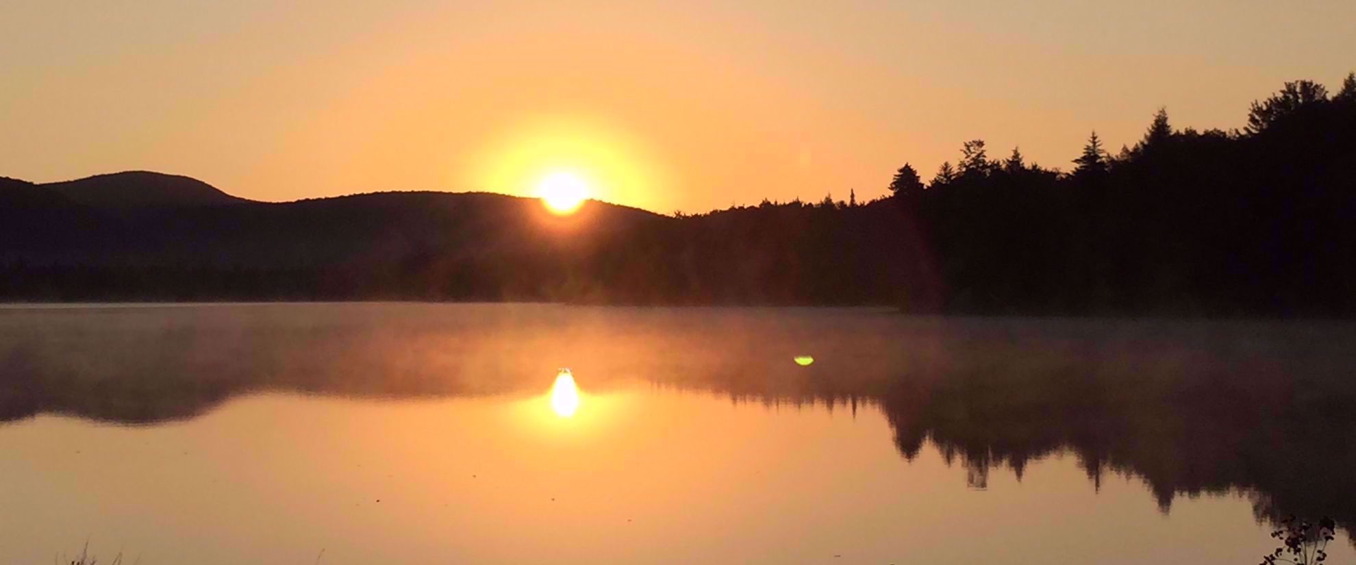 Golden sunset behind Adirondack mountain ridge by lake