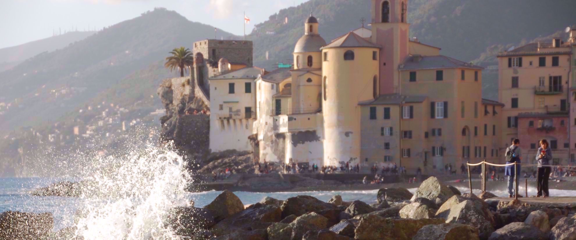 Waves crashing on rocks in italy with old building in background