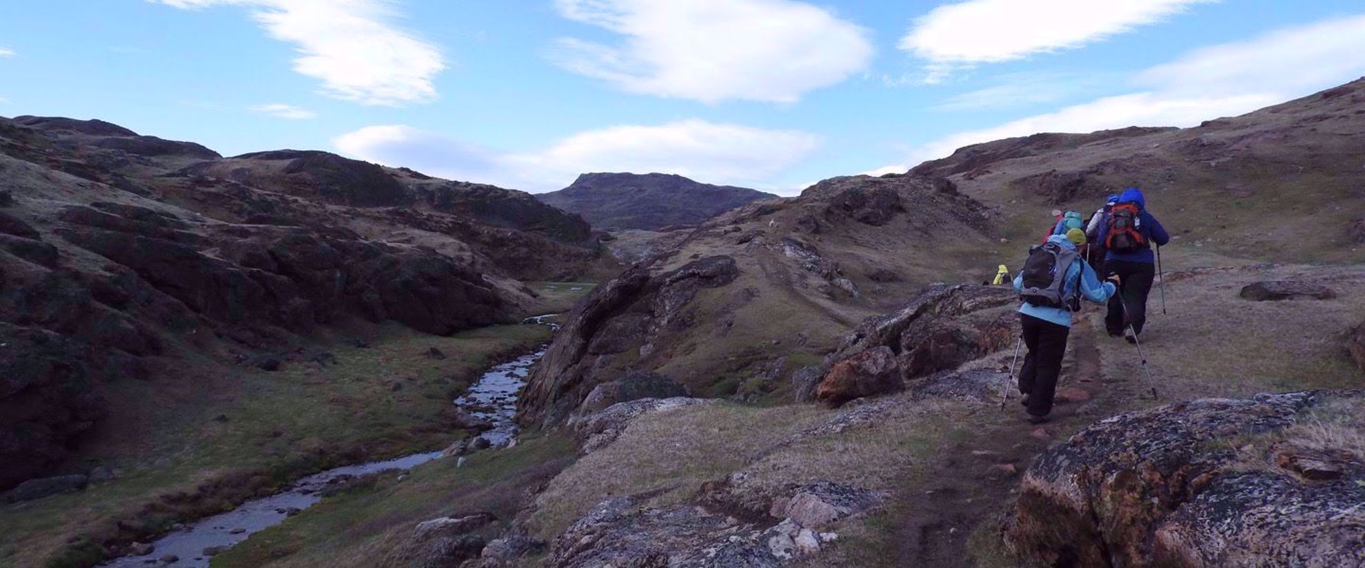 women hiking by stream on trail in greenland