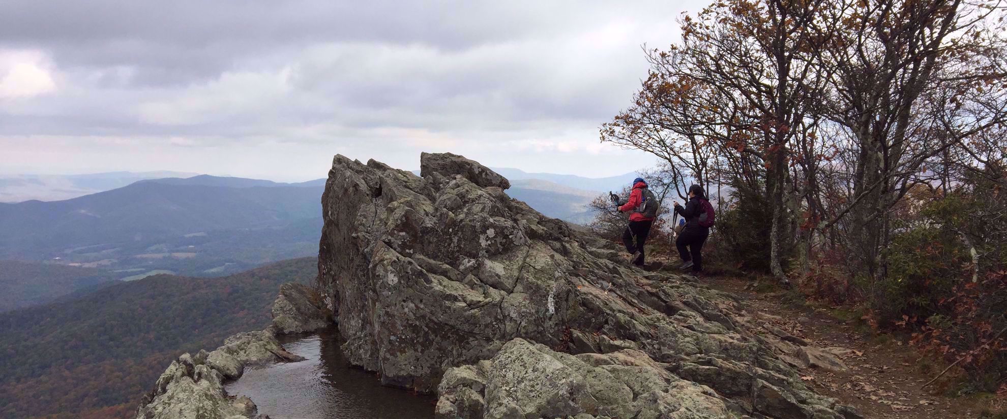 women hike mountain with small pond