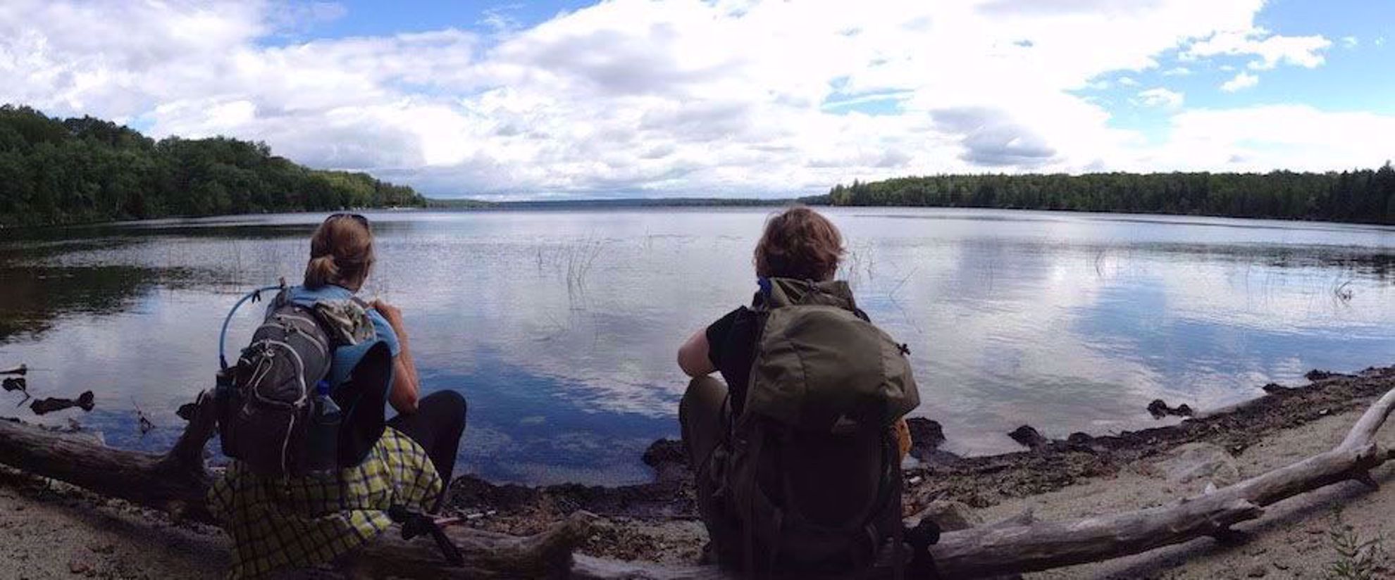 women relax by water while hiking through maine