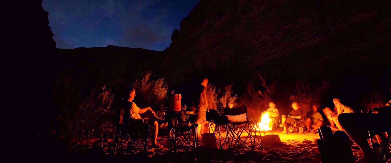 Cataract Canyon group sitting around campfire at night, silhouettes in darkness