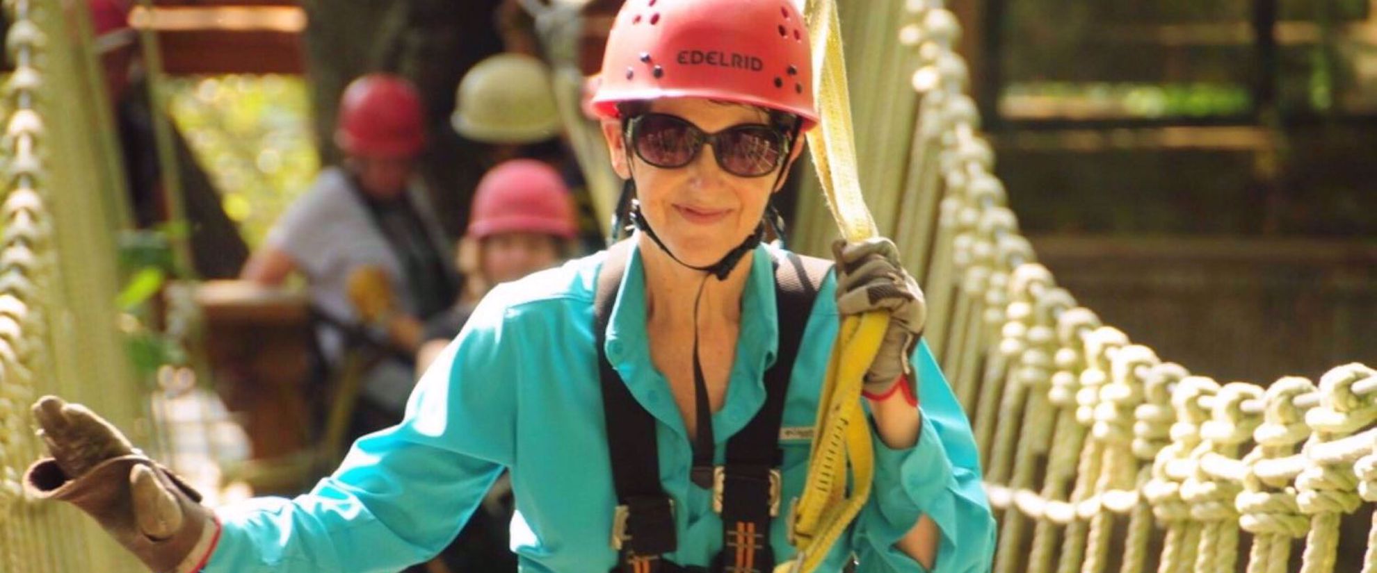 Picture of Blue Ridge Rambling Woman crossing suspension bridge, smiling with red helmet